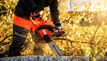 A close-up photo of a Husqvarna chainsaw cutting through a fallen tree with bright yellow foliage.
