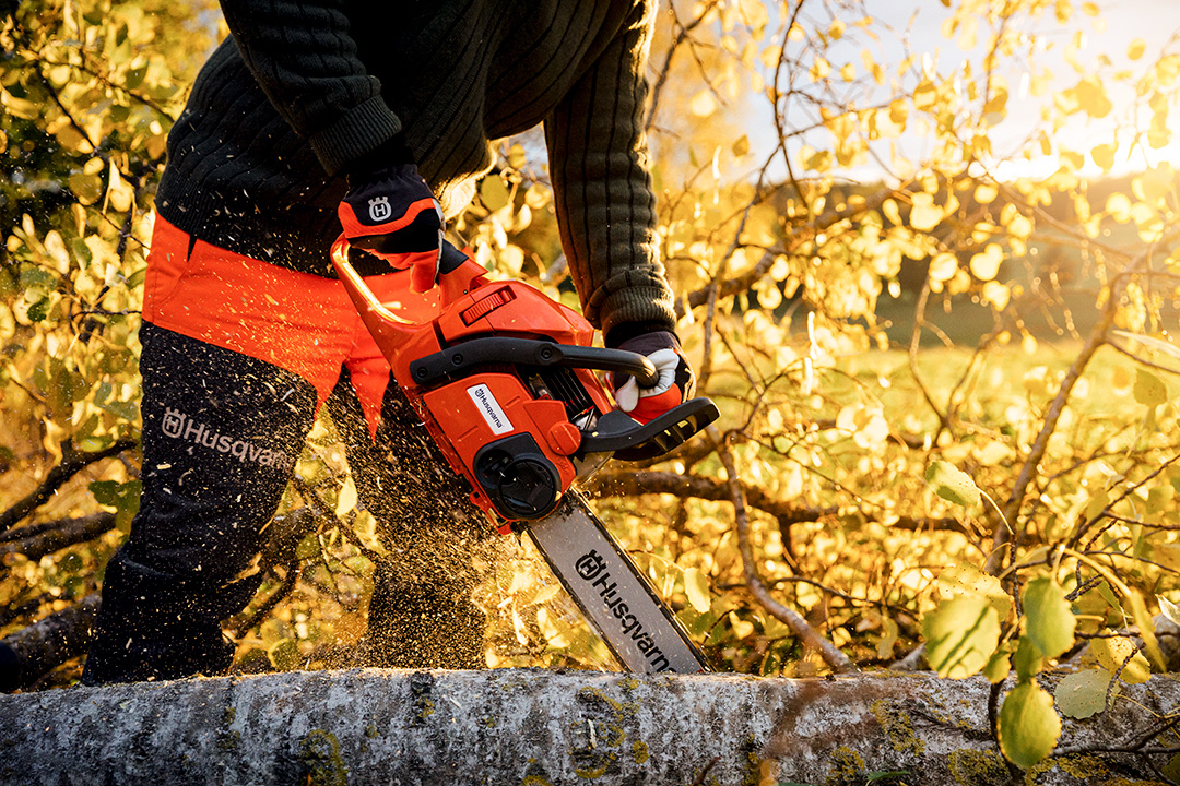 A close-up photo of a Husqvarna chainsaw cutting through a fallen tree with bright yellow foliage.