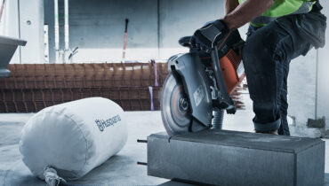 A Husqvarna power cutter being used to cut a large conrete slab on a construction site, with a Husqvarna dust collector in the background.