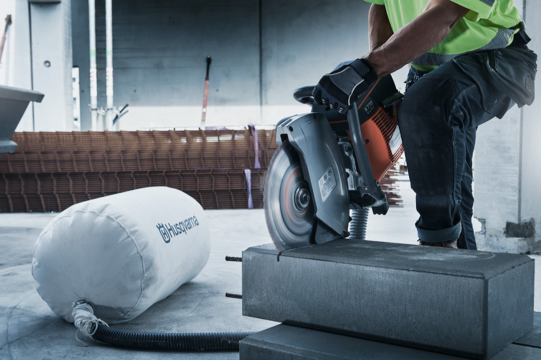 A Husqvarna power cutter being used to cut a large conrete slab on a construction site, with a Husqvarna dust collector in the background.