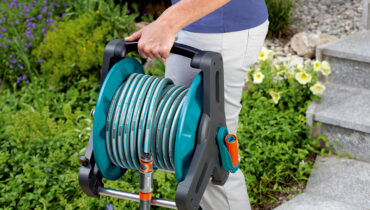 A man holding a GARDENA hosepipe reel while walking through a lush garden.