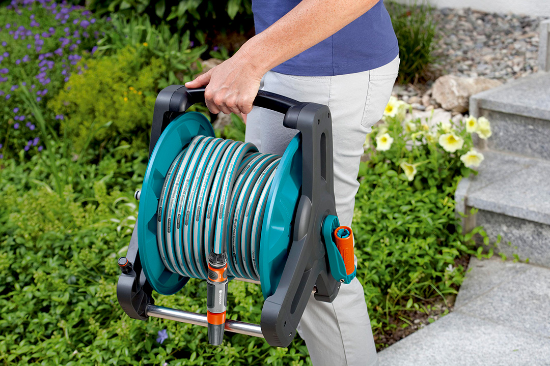 A man holding a GARDENA hosepipe reel while walking through a lush garden.