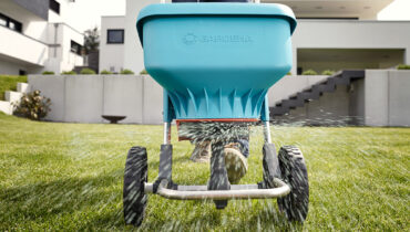 A GARDENA spreader XL being used to disperse fertiliser on a healthy, green lawn.