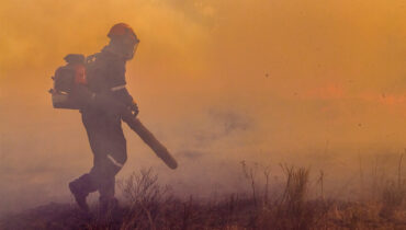A man holding a Husqvarna firefighting blower in a smoky field.