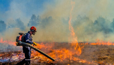 A man walking through a burning field using a Husqvarna blower as a firefighting tool.