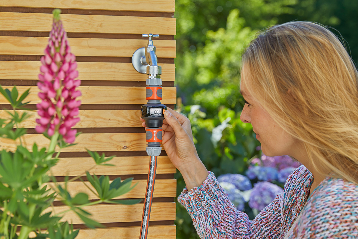 A woman looking at her GARDENA AquaCount water meter for water management.