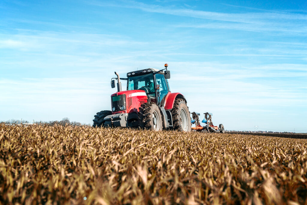 A red tractor pulling a plough through a maize field.