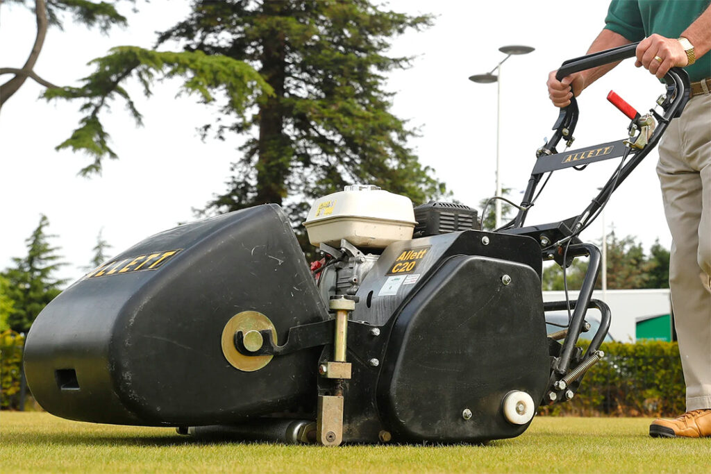 A man pushing an Allett C20 cylinder mower across a golf course green.