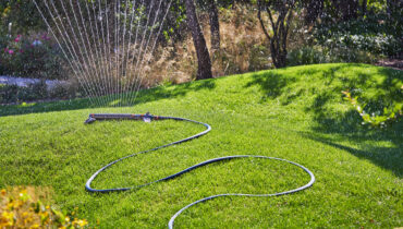 A GARDENA Oscillating Sprinkler on a green lawn with a blue hose pipe.