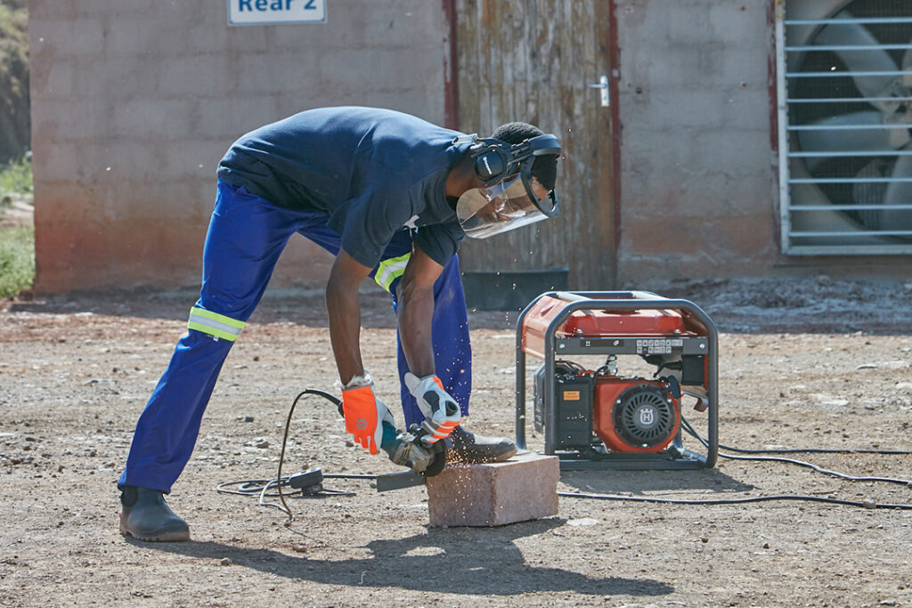 A worker using a Husqvarna generator to power his angle grinder on a farm.
