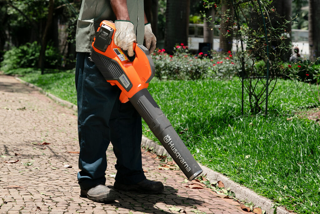 A man holds a Husqvarna battery leaf blower to blow leaves from a path.