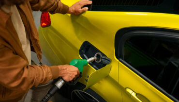An unidentified man fills up his yellow car with fuel from a green petrol pump.
