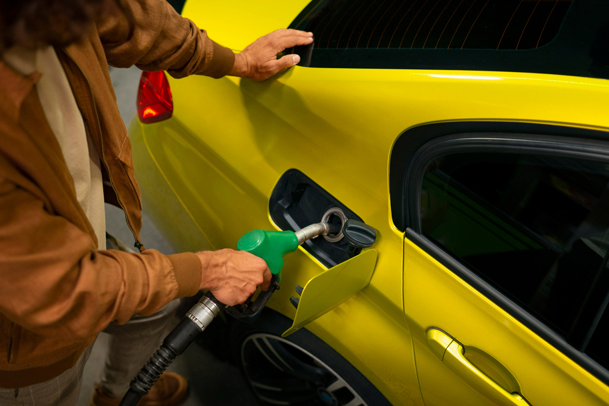 An unidentified man fills up his yellow car with fuel from a green petrol pump.