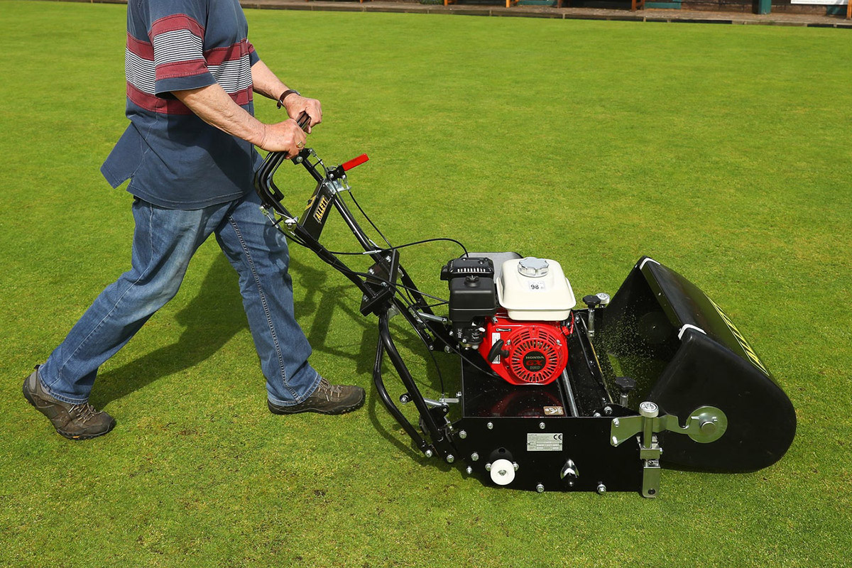 A man pushing an Allett cylinder mower on a manicured green turf